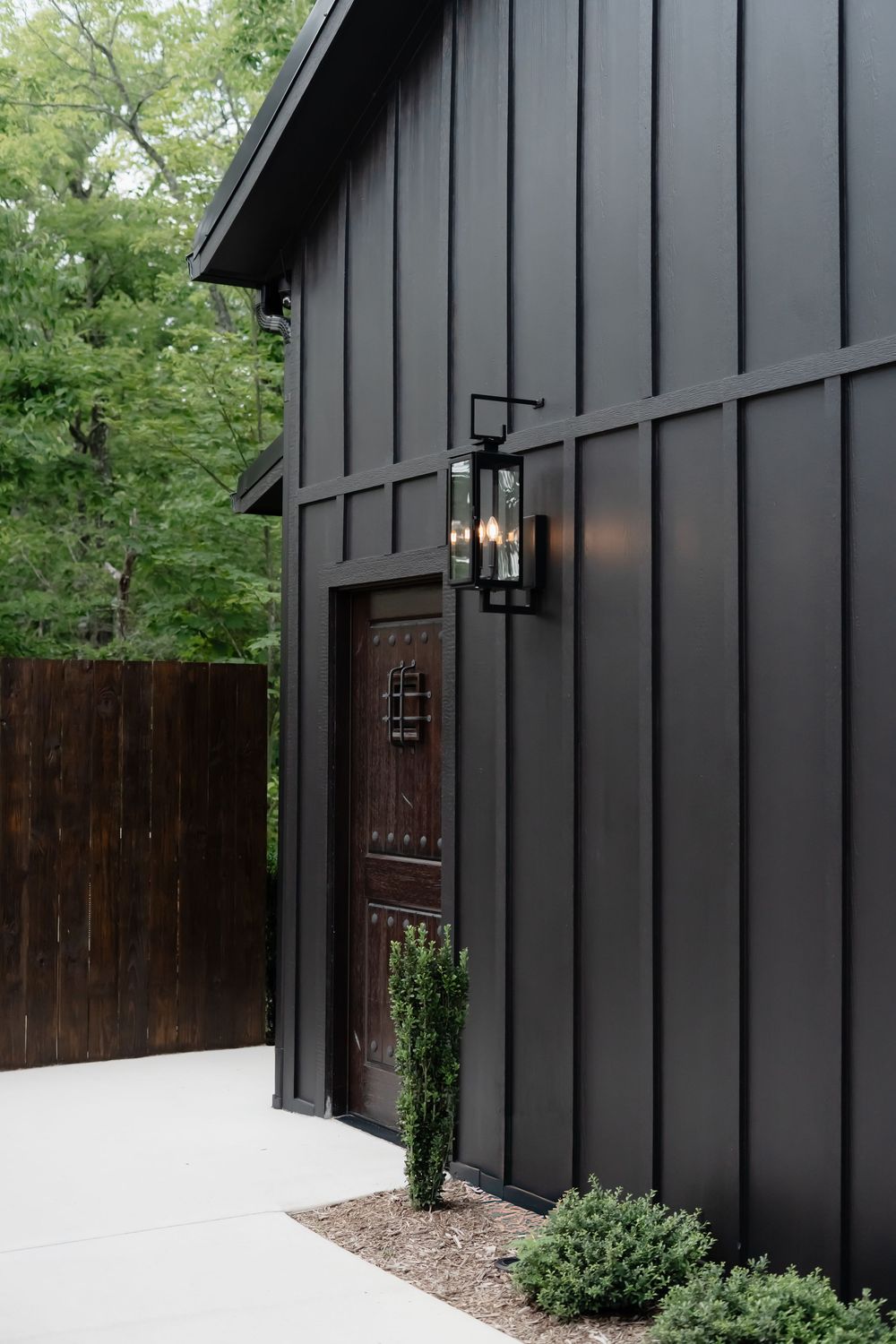 Modern black barn-style building exterior with wooden door and black lantern wall sconce.