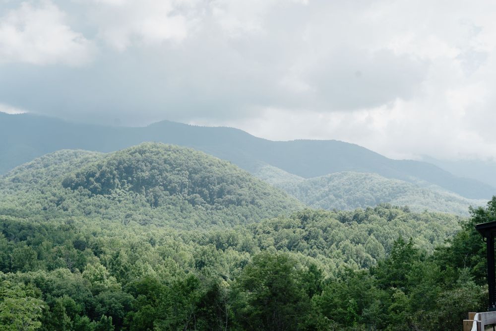 Panoramic view of rolling green forested mountains under a cloudy sky.