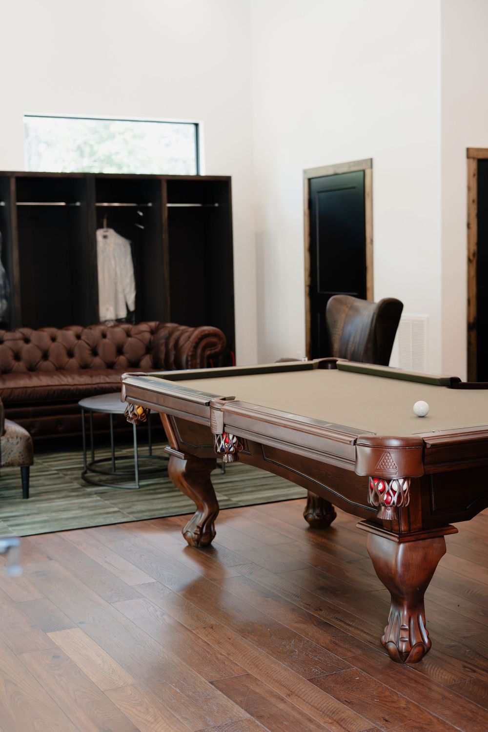 Elegant billiard room with ornate wooden pool table, leather Chesterfield sofa, and hardwood floors in a modern space.