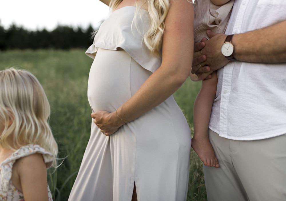 A family during a maternity session outdoors in a green field.