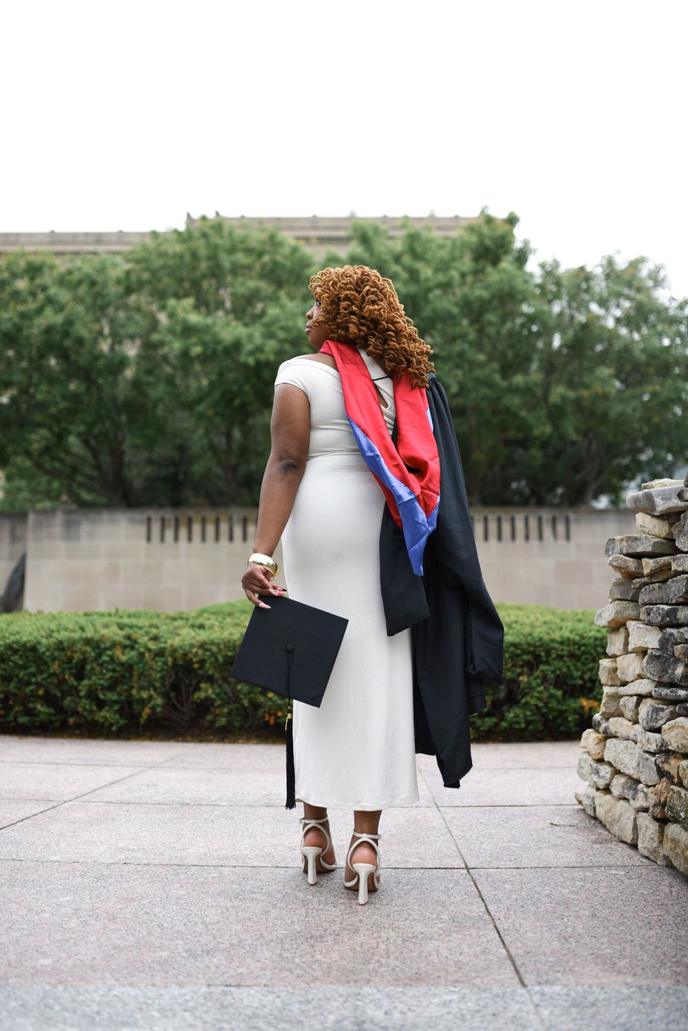 A graduate celebrating her master's degree during a graduate session with an outdoors scenic view.