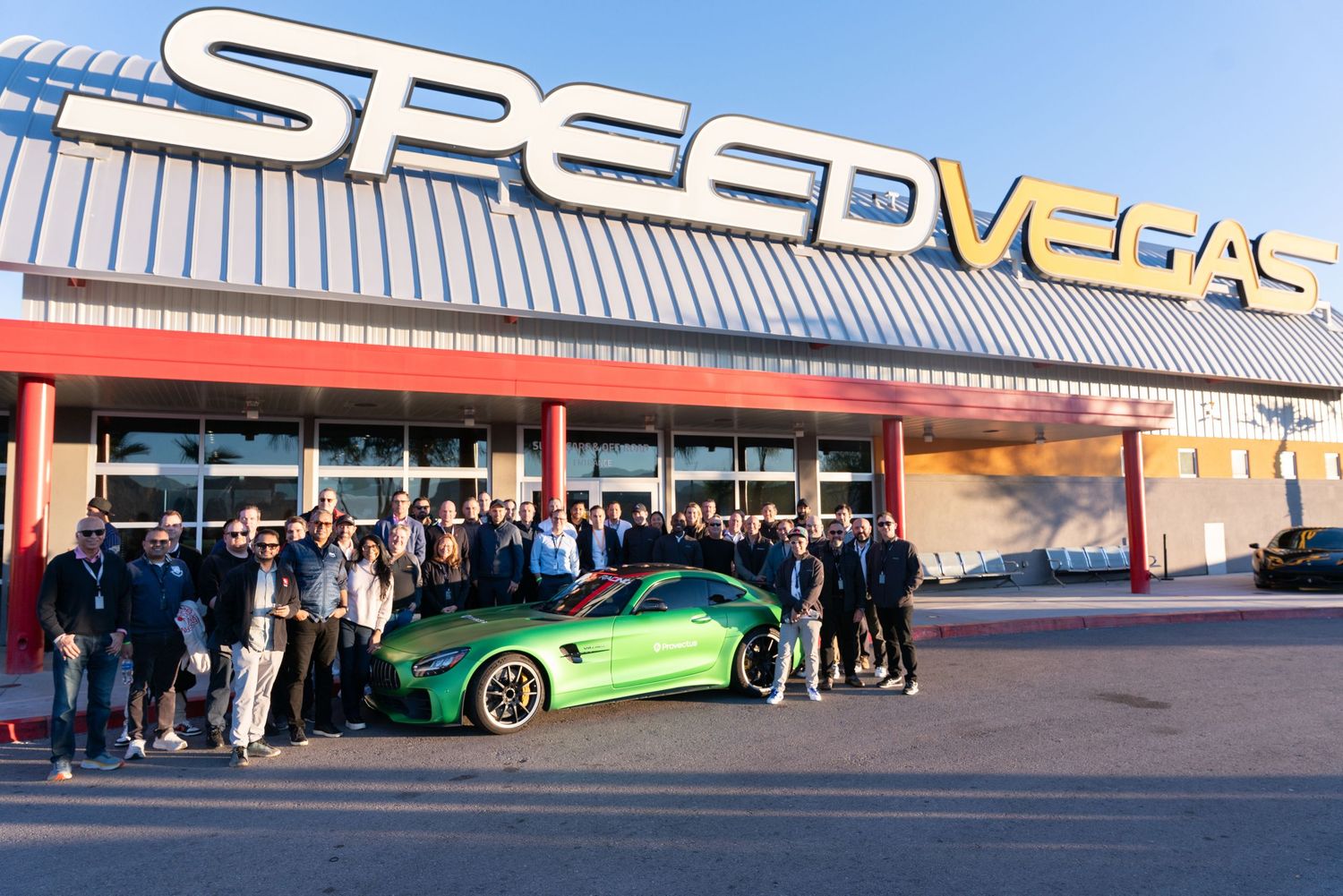 Group of people posing in front of a green sports car at SpeedVegas racing experience center.