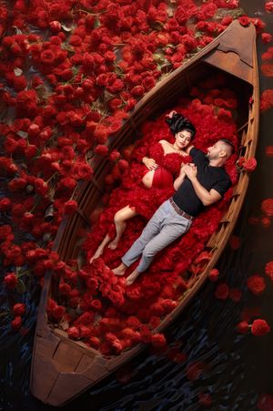 Glamorous couple: mum-to-be and husband laying together in a luxurious red rose river digital scene.