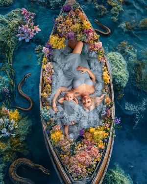 Fine art portrait of a mother and daughter floating down a river in a flower filled boat, both in matching luxury gowns.