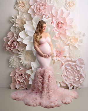 Glowing pregnancy portrait: mum-to-be wearing a soft peach gown against a white, cream and peach flower wall by Caz Captures Sydney.