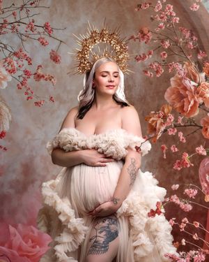 Elegant cream maternity gown, against flower branches and sunbeams perfect for a timeless studio portrait.