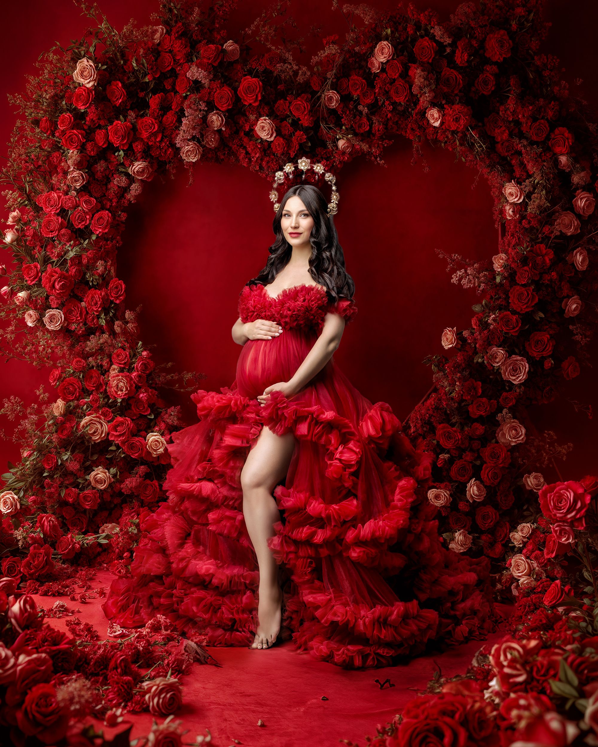 Woman in red couture gown against stunning red heart wall of red flowers she wear a gold flower crown and looks breathtaking.