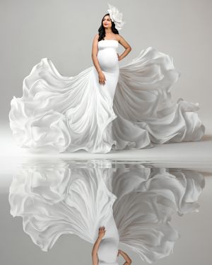 A minimalistic maternity portrait of a woman all in white her gown floating up around her, and reflected in the water before her.
