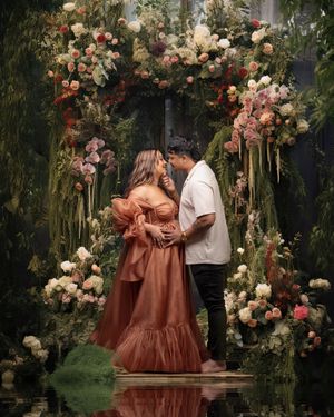A glamorous maternity couple sharing an intimate moment surrounded by a dreamy romantic lush tropical forrest arch.