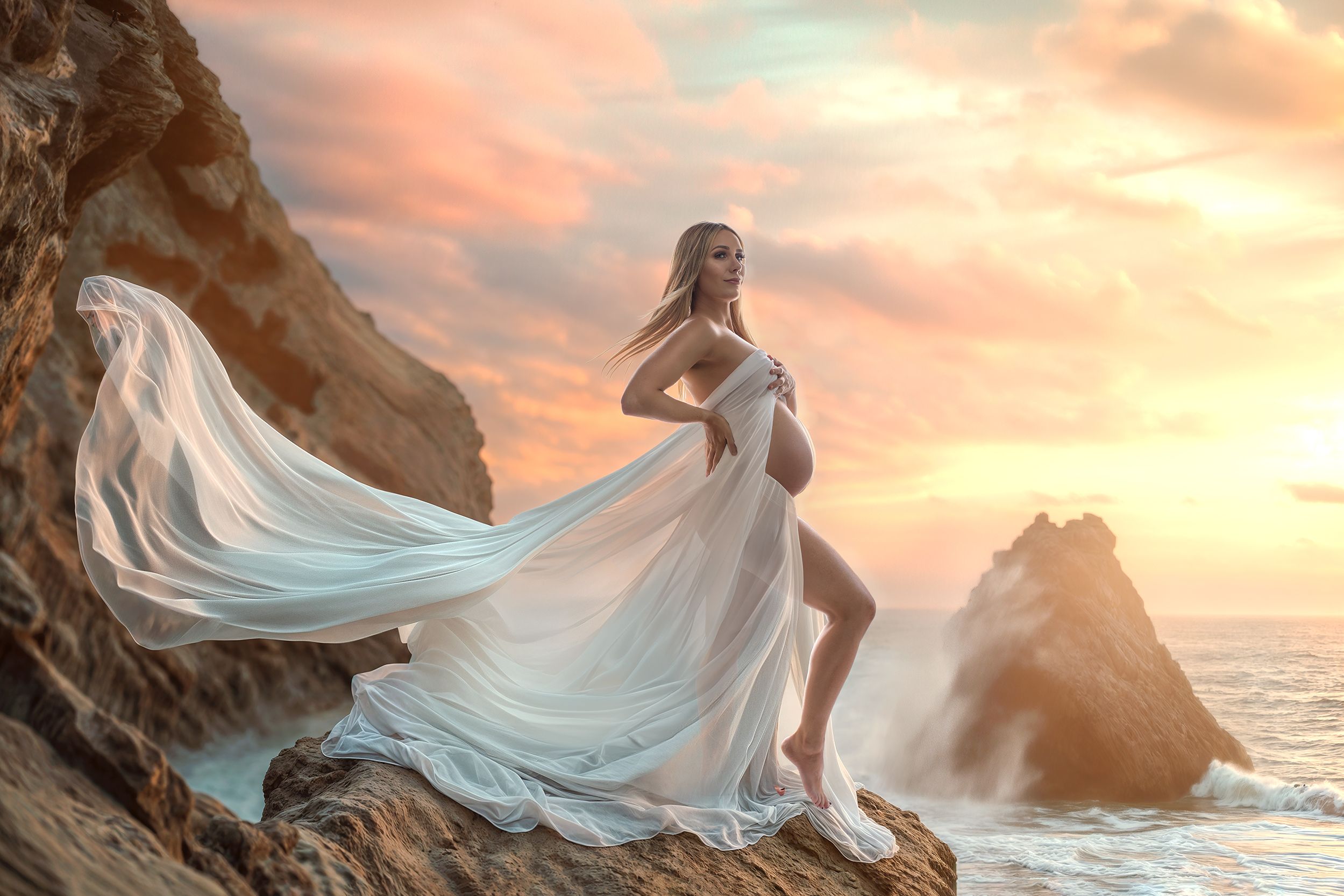 Maternity portrait of a windswept woman standing on a rock against the sunset over looking the water. Giving Goddess.