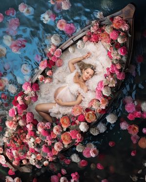 Professional Sydney photographer Caz Captures: pregnant woman floating in a river of pink and cream flowers wearing elegant cream gown.