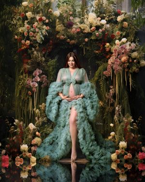 Mum-to-be in an green gown, posed against a rich, dark green tropical digital arch backdrop.