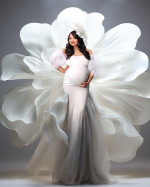 Fine art maternity photo of a woman in an elegant white couture gown and hat against a dramatic large white flower.