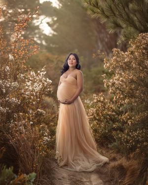 A mother-to-be holds her belly standing in a golden garden setting.
