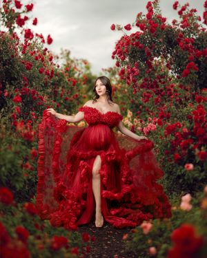 Pregnant mumma wearing red couture gown swishing her gown in a garden of red flowers.