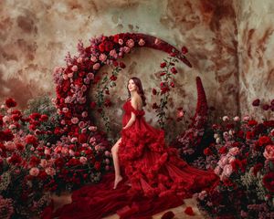 Romantic maternity portrait woman in a designer gown looks beautiful against whimsical red rose garden.