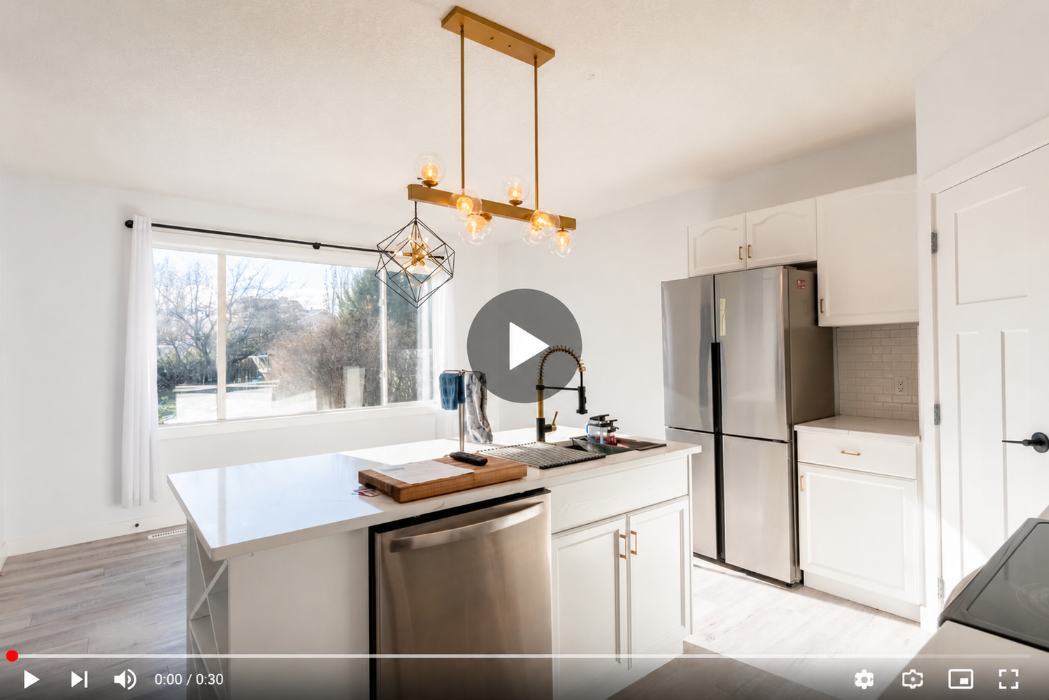 Modern kitchen with white cabinets, gold pendant light, stainless steel appliances, and large window overlooking backyard.