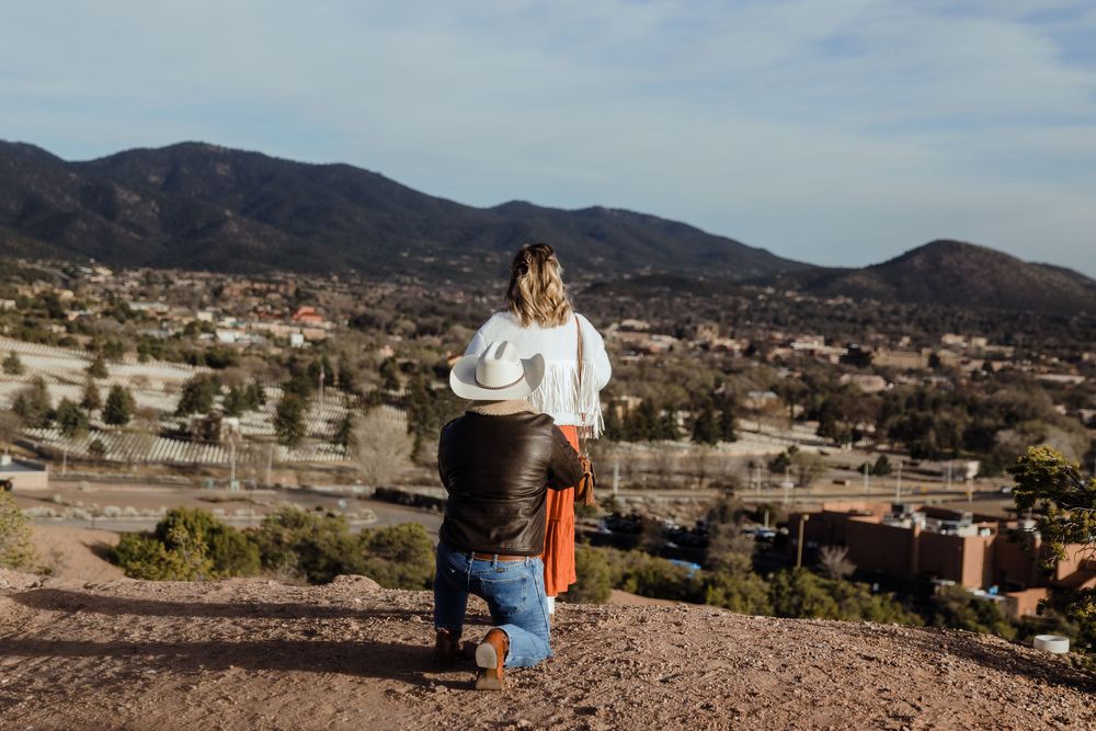 Couple on hilltop overlooking a scenic mountain town landscape under a clear blue sky.