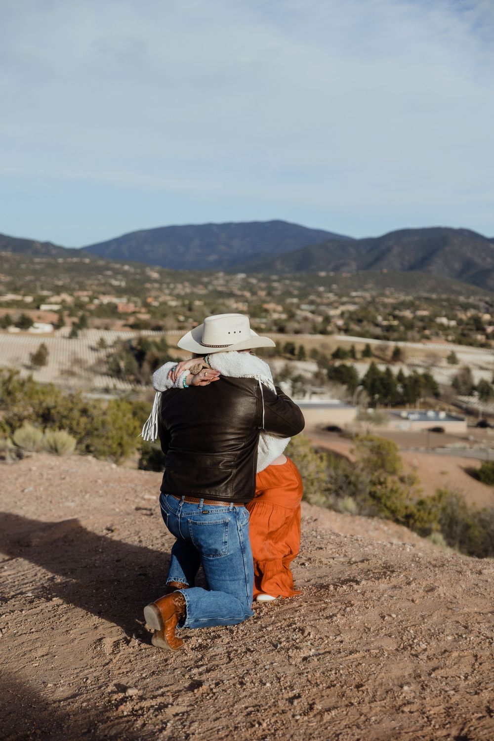 Couple embracing on a hilltop overlook with scenic desert mountains and valley views in the background.