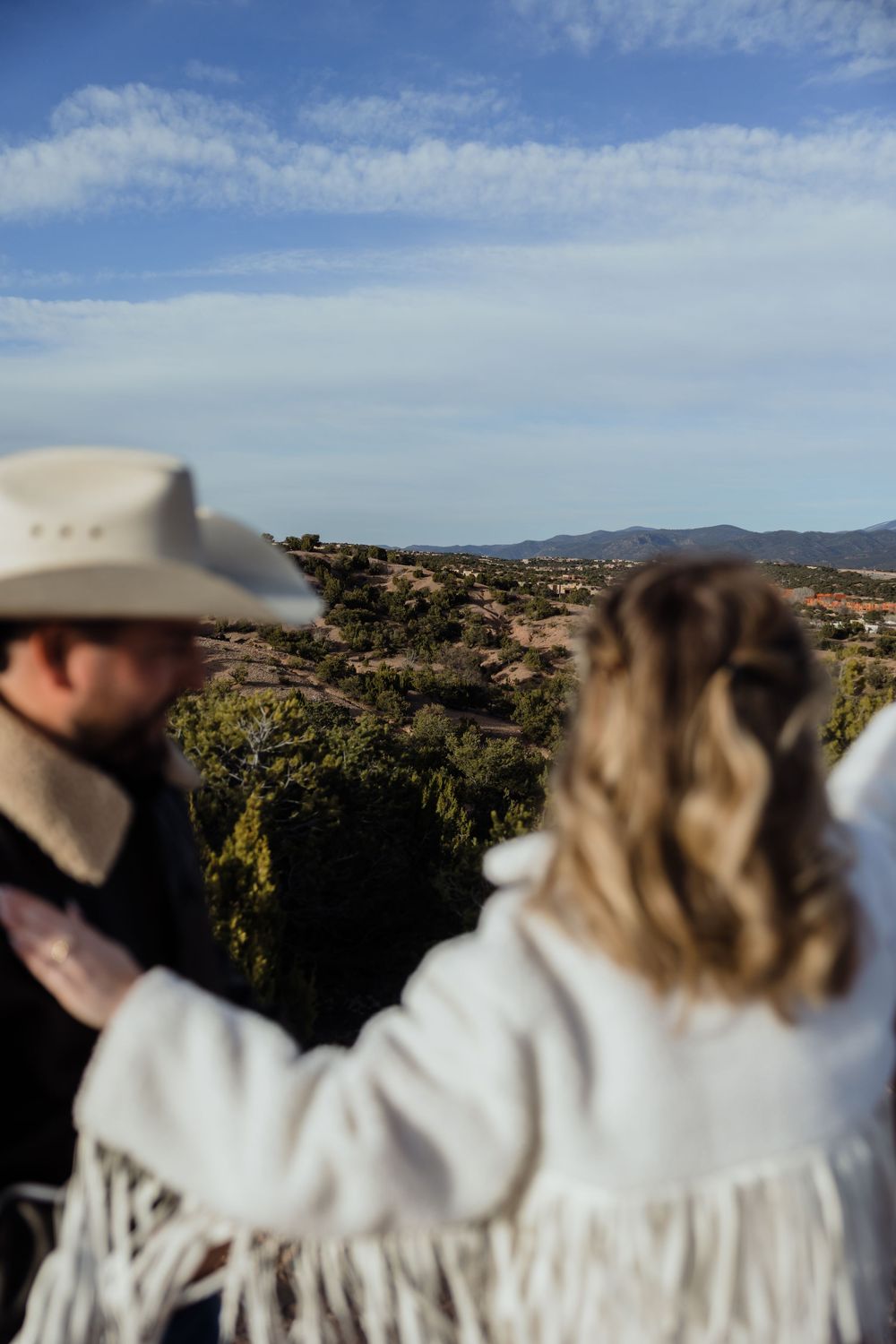 Couple standing together overlooking a vast desert landscape with mountains and blue sky.