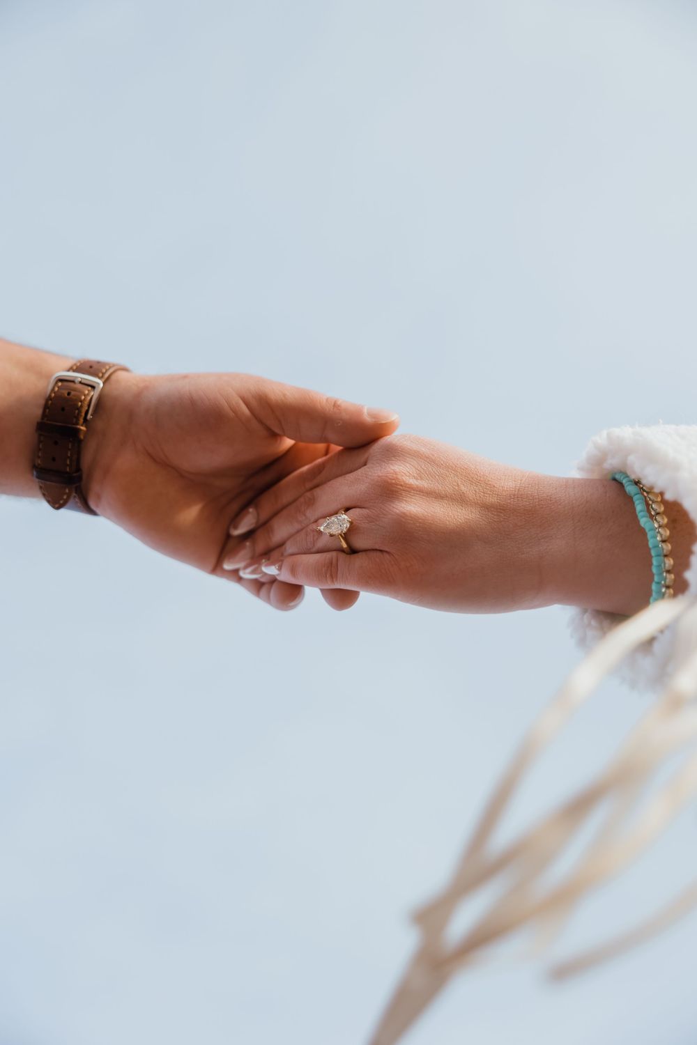 Close-up of an engaged couple holding hands, showcasing a diamond engagement ring and turquoise bracelet.