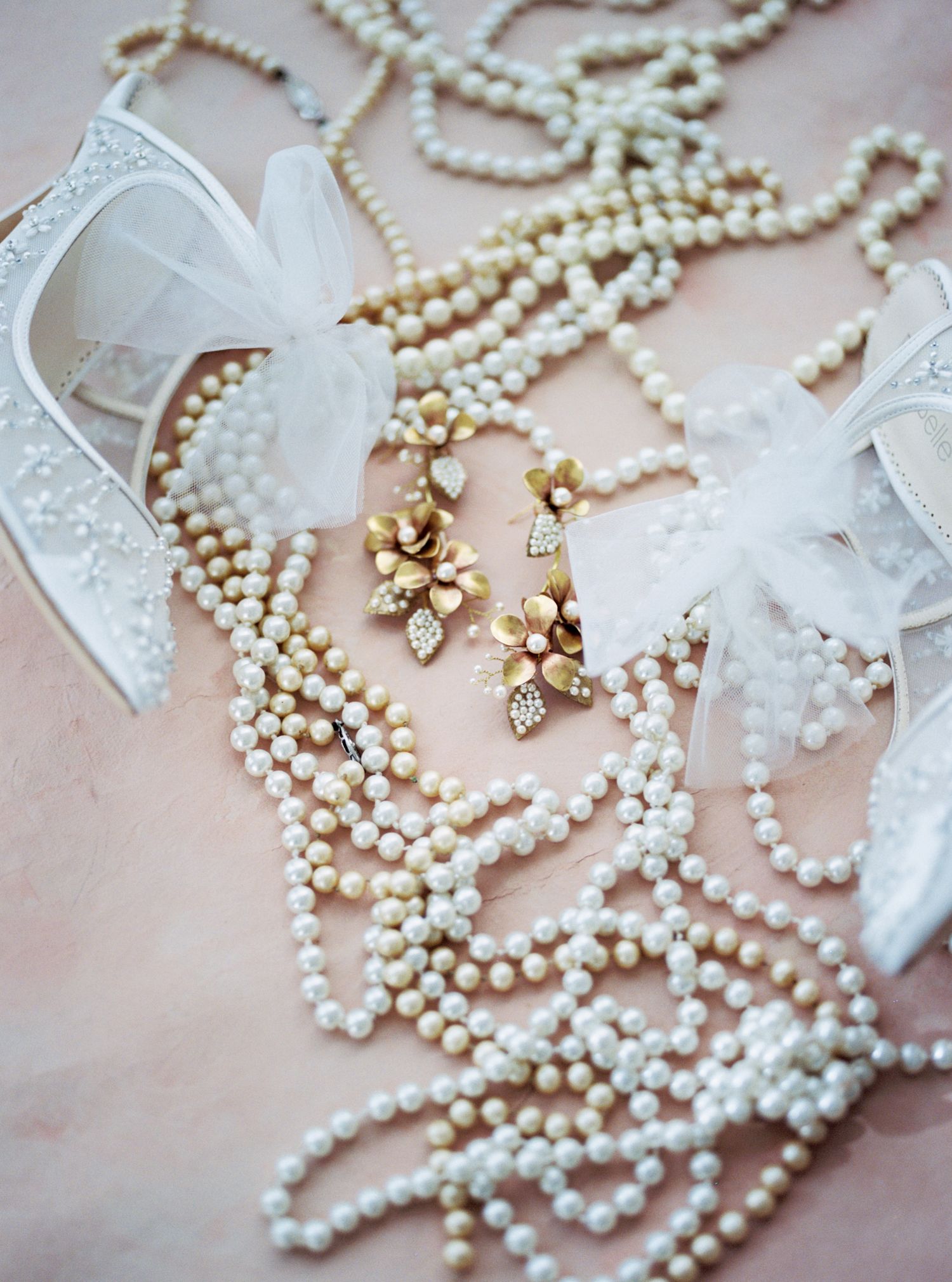 Delicate pearl necklace with white organza bows and crystal earrings arranged on pink background for bridal accessories.