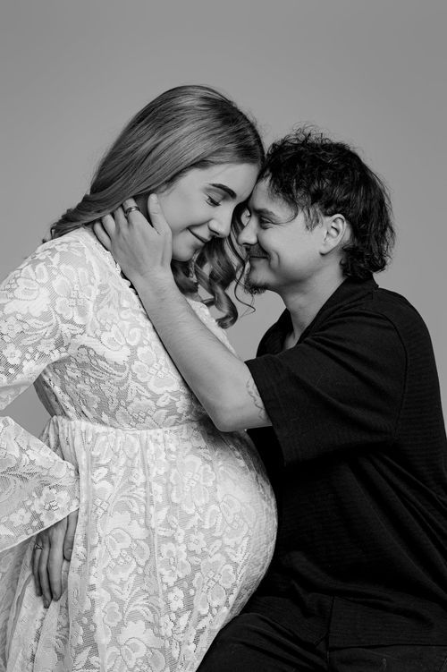 Black and white maternity photo of couple sharing tender forehead touch in studio.