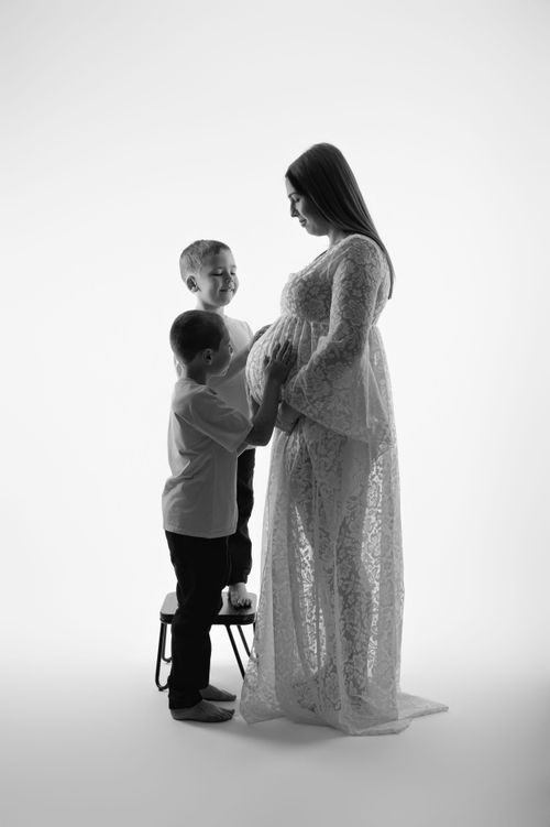 Black and white maternity photo of pregnant woman in lace gown with two young sons.