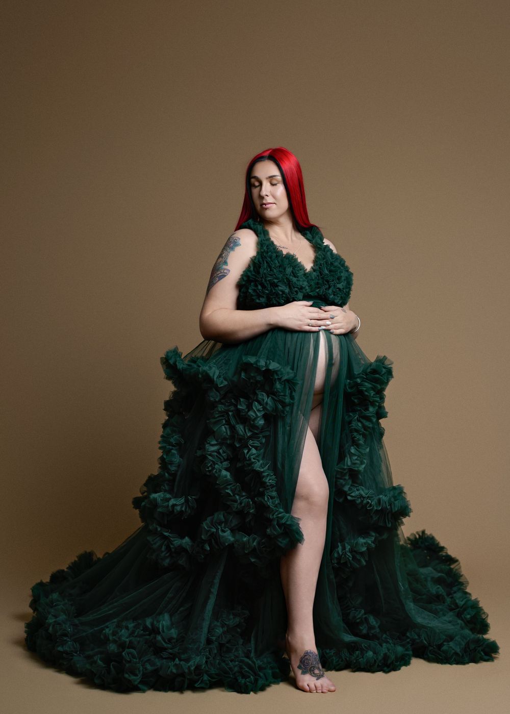 Pregnant woman in elegant dark green ruffled tulle maternity gown with red hair, posing gracefully in studio,