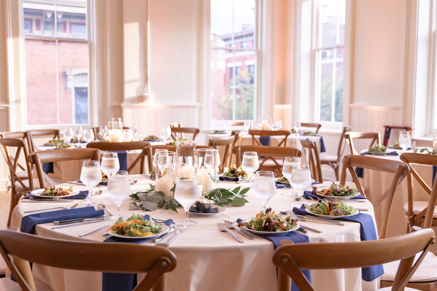 Elegant round dining table set with blue napkins, salad plates, and wine glasses in The Alcove Cincinnati.