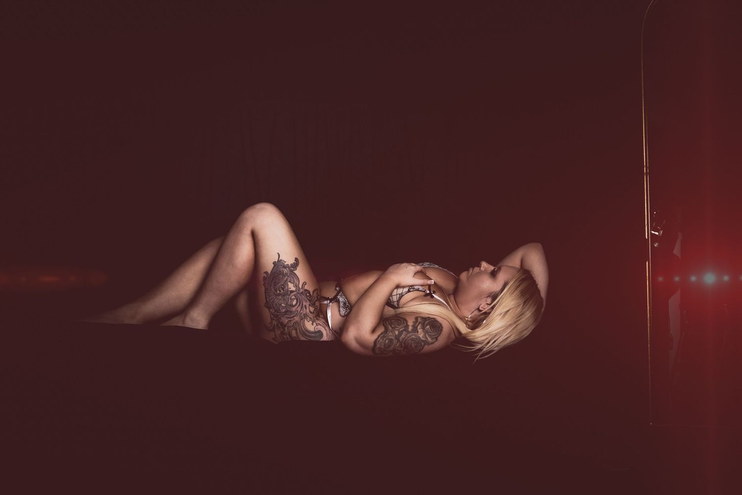 A person lies on a dark red surface in dramatic lighting wearing a lace outfit.