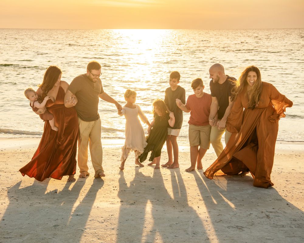 Sibling families gathered on a Dunedin, Florida beach at sunset, capturing a joyful multi-family portrait by the Gulf.