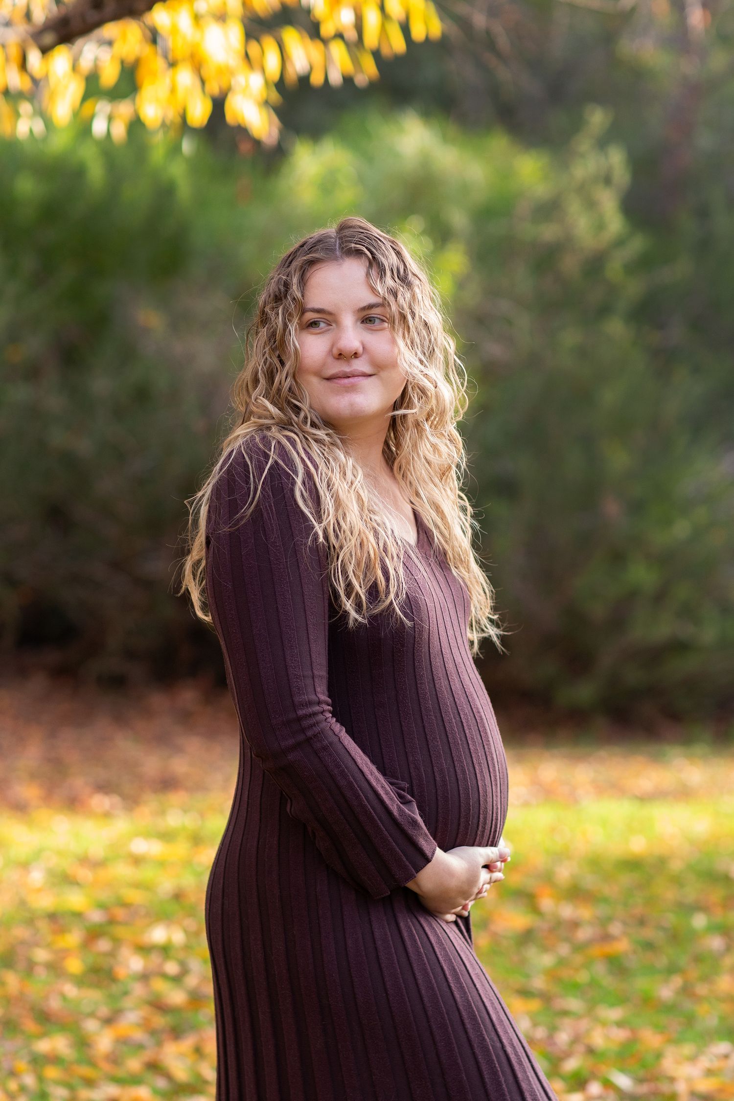 Mother to be embracing her bump in perth during a maternity photo session at golden hour in autumn