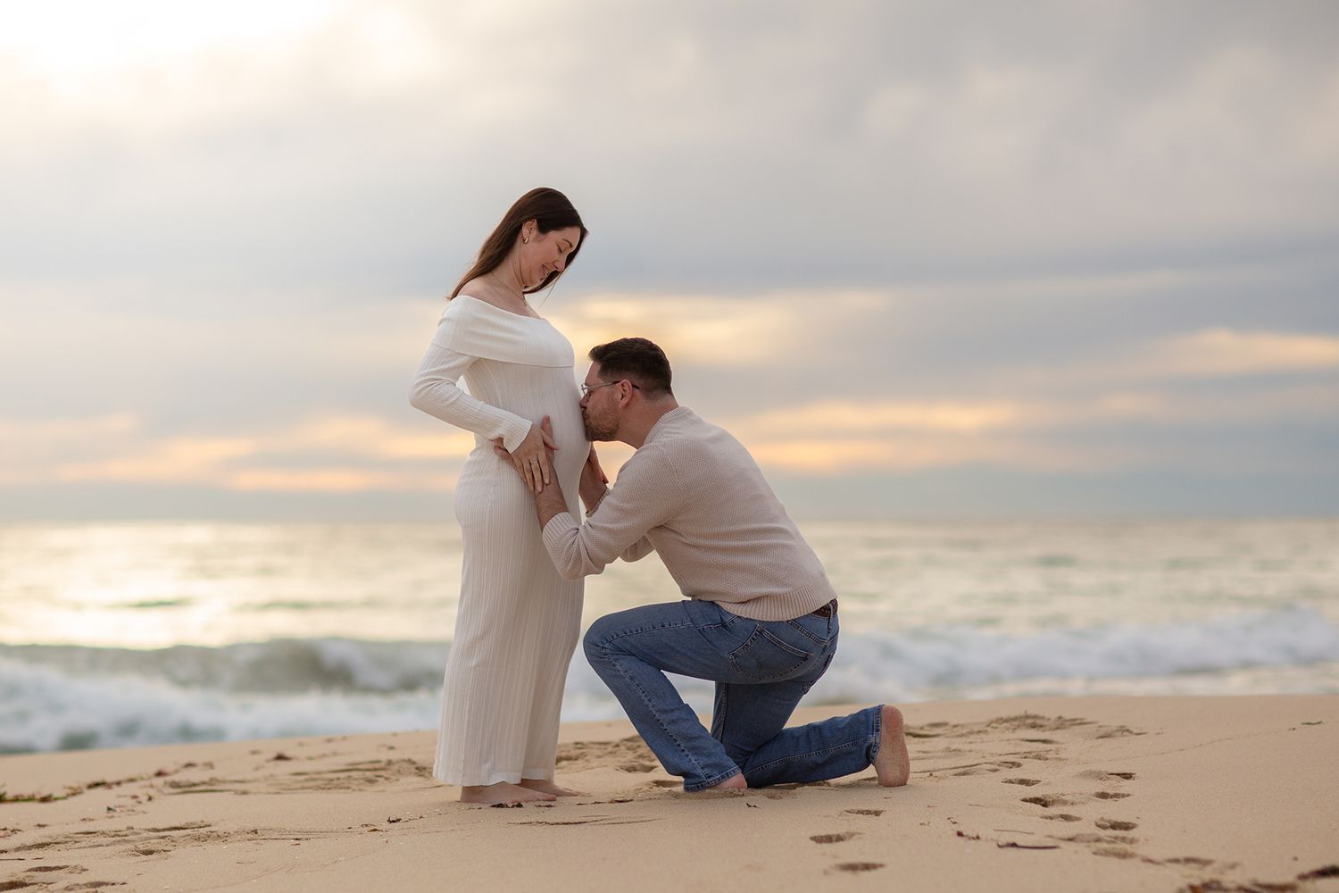 Father to be kissing belly of his wife during their maternity shoot at sunset on the beach in perth