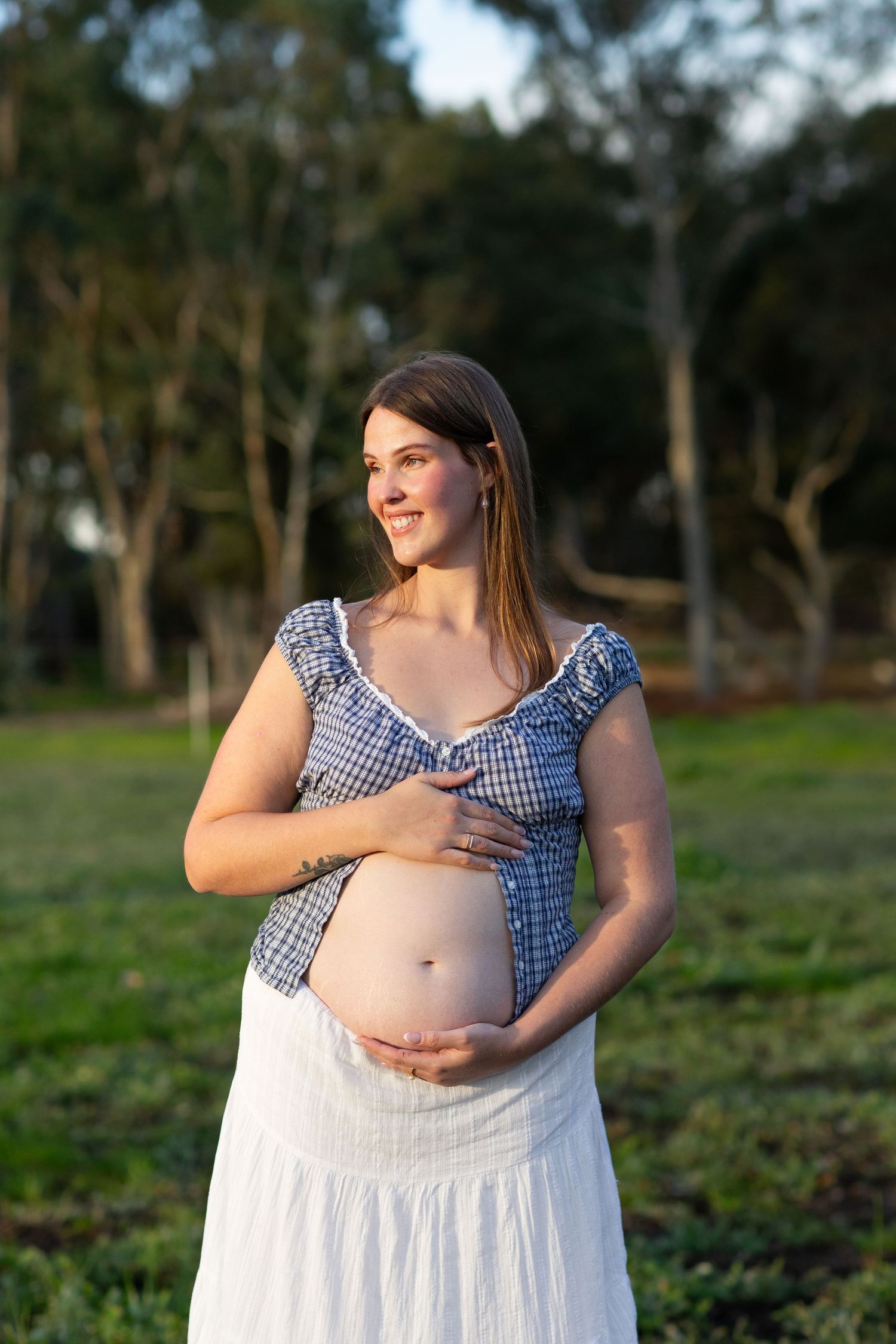 Mum to be holding baby bump in an open paddock at golden hour during a maternity session in Perth