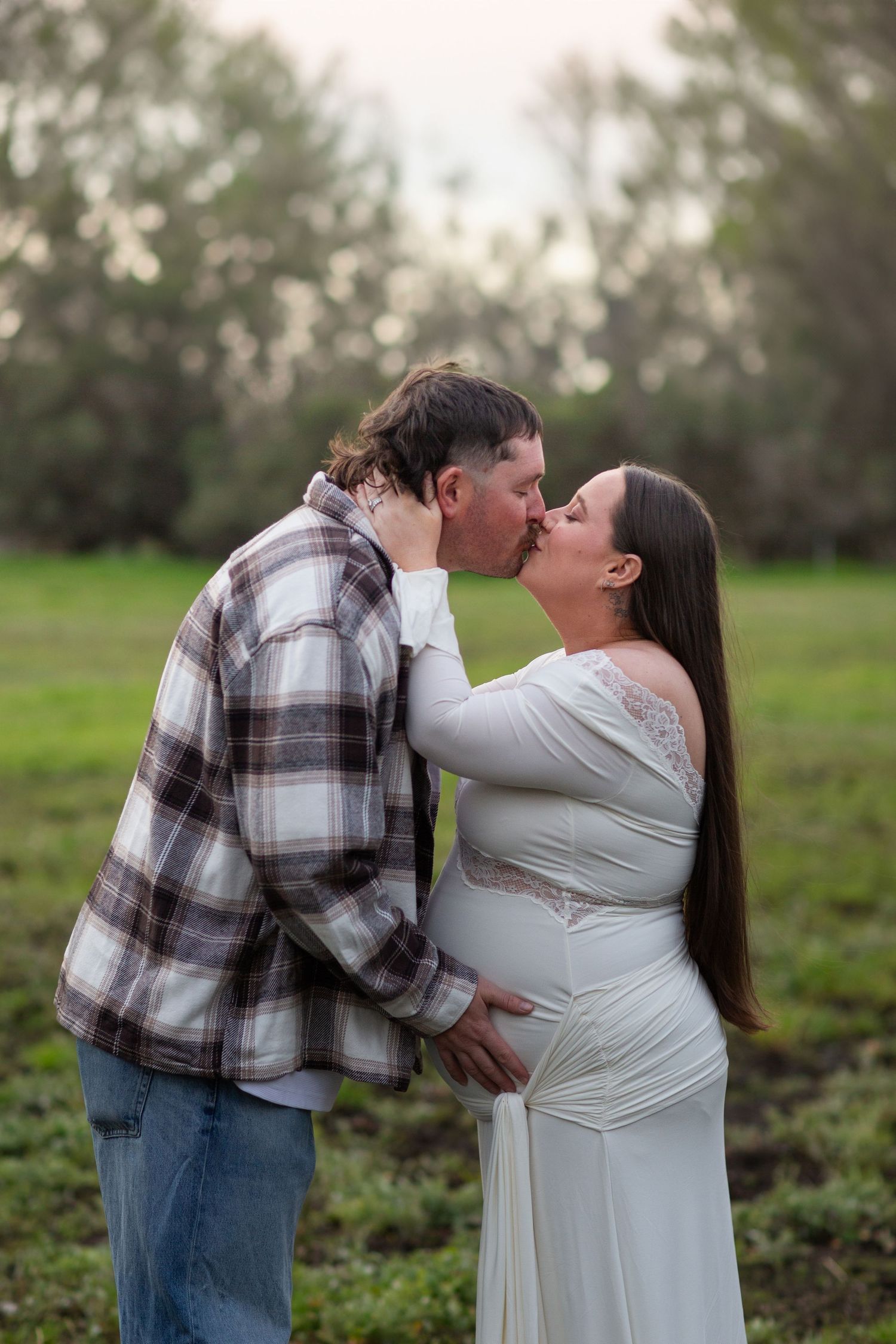 Couple sharing a kiss while holding baby bump on a rural property during a maternity photo session in Perth