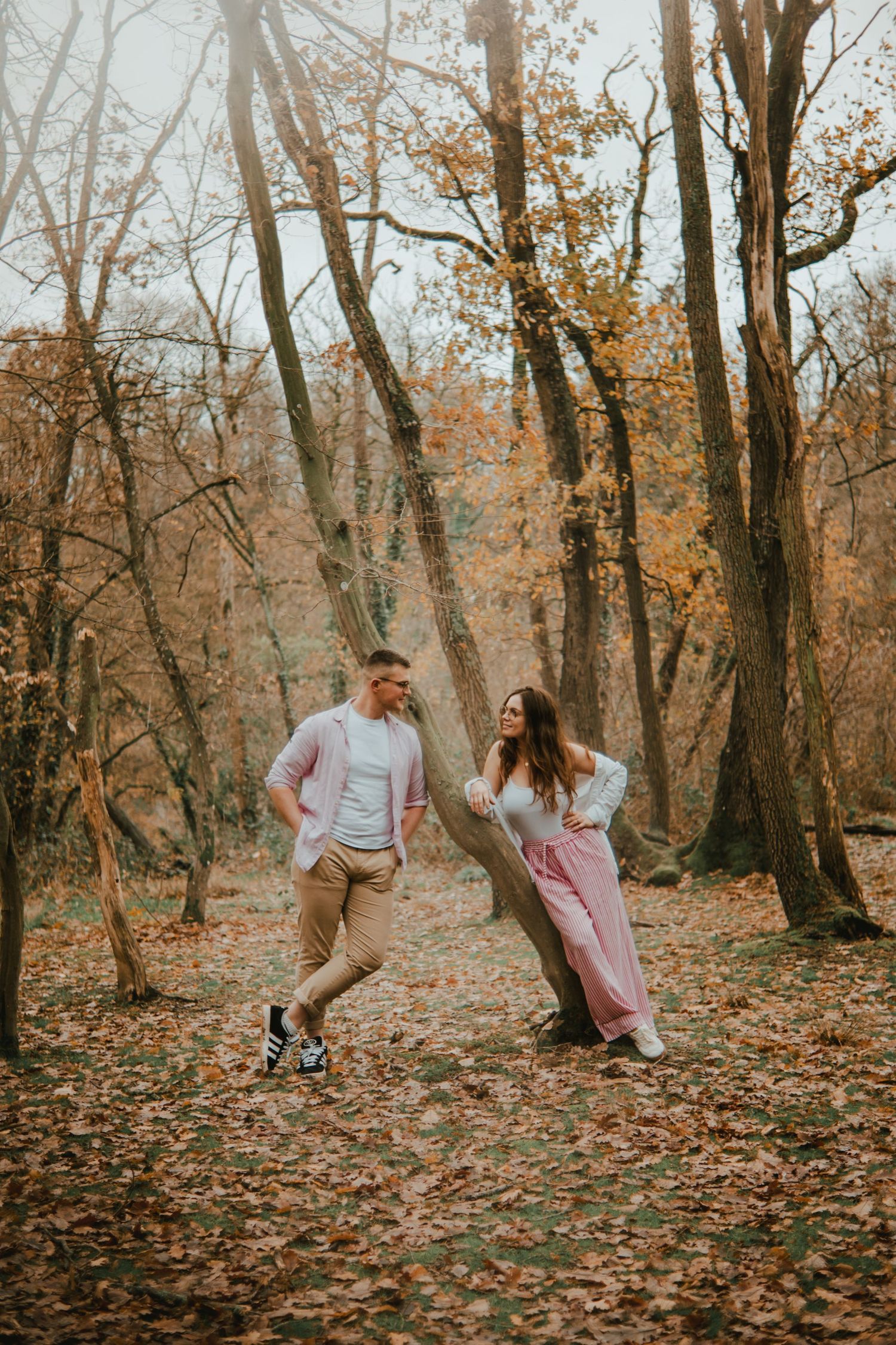 Couple enjoying a romantic autumn walk in a colorful fall forest, surrounded by golden leaves and tall trees.