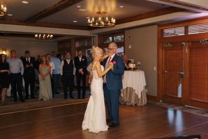 Bride and father share first dance at elegant wedding reception while guests watch in warmly lit venue.