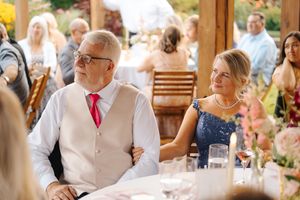 Couple in formal attire sitting together at an outdoor wedding reception, man in vest and red tie, woman in blue sequin dress.