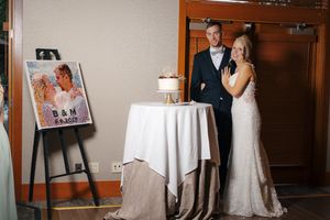 Bride and groom standing beside wedding cake and personalized B&M sign at elegant indoor reception venue.