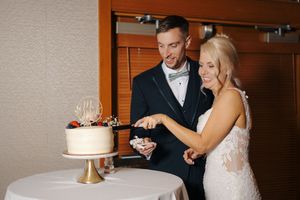 Bride and groom smiling while cutting their elegant white wedding cake together at their reception.