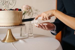Newlyweds cutting a white wedding cake on a gold stand, adorned with fresh berries and a Mrs. cake topper.