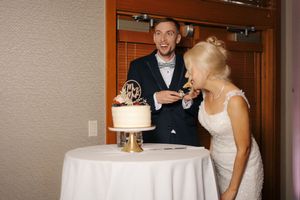Bride and groom laughing while cutting their white wedding cake at their wedding reception.