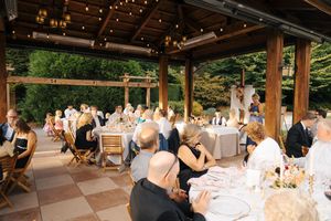 Guests seated at elegant outdoor wedding reception under wooden pergola with string lights at golden hour.