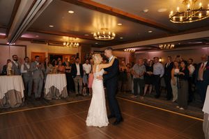 Bride and groom share their first dance surrounded by wedding guests in a chandelier-lit ballroom.