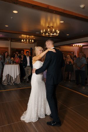 Bride and groom share their first dance at wedding reception, surrounded by guests in elegant wood-paneled ballroom.