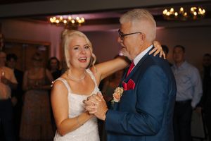 Bride shares a joyful father-daughter dance with her dad in a blue suit at wedding reception.