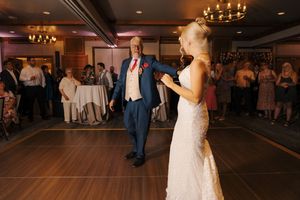 Bride in lace gown dances with father in blue suit during wedding reception father-daughter dance.