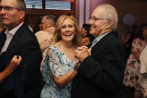 Elderly couple dancing together at a formal event, smiling joyfully on a crowded dance floor.