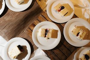 Aerial view of white plates with slices of layered cake topped with berries on a wooden table.